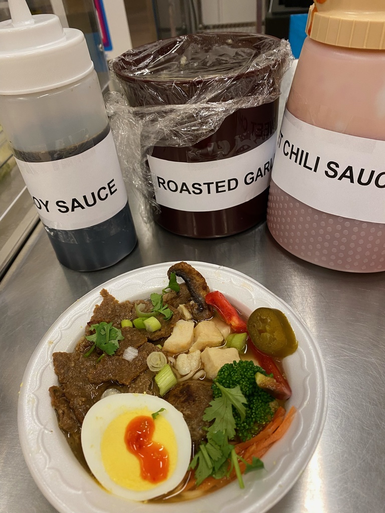 a bowl filled with noodles, meat, egg, and veggies. Also icnludes containers of difference sauces