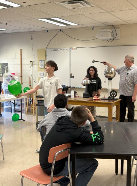 Students and a teacher in a science classroom doing an experiment with different sized metal balls