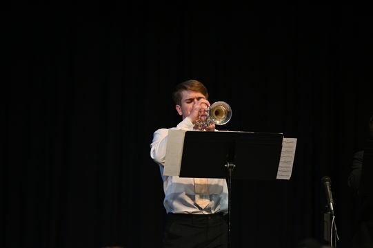 Male student playing the trumpet with a music stand in front of him.