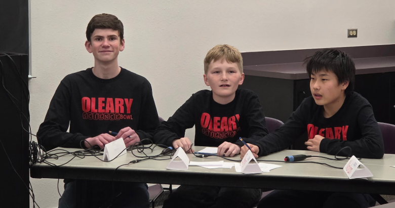Three kids sitting at a table for the competition