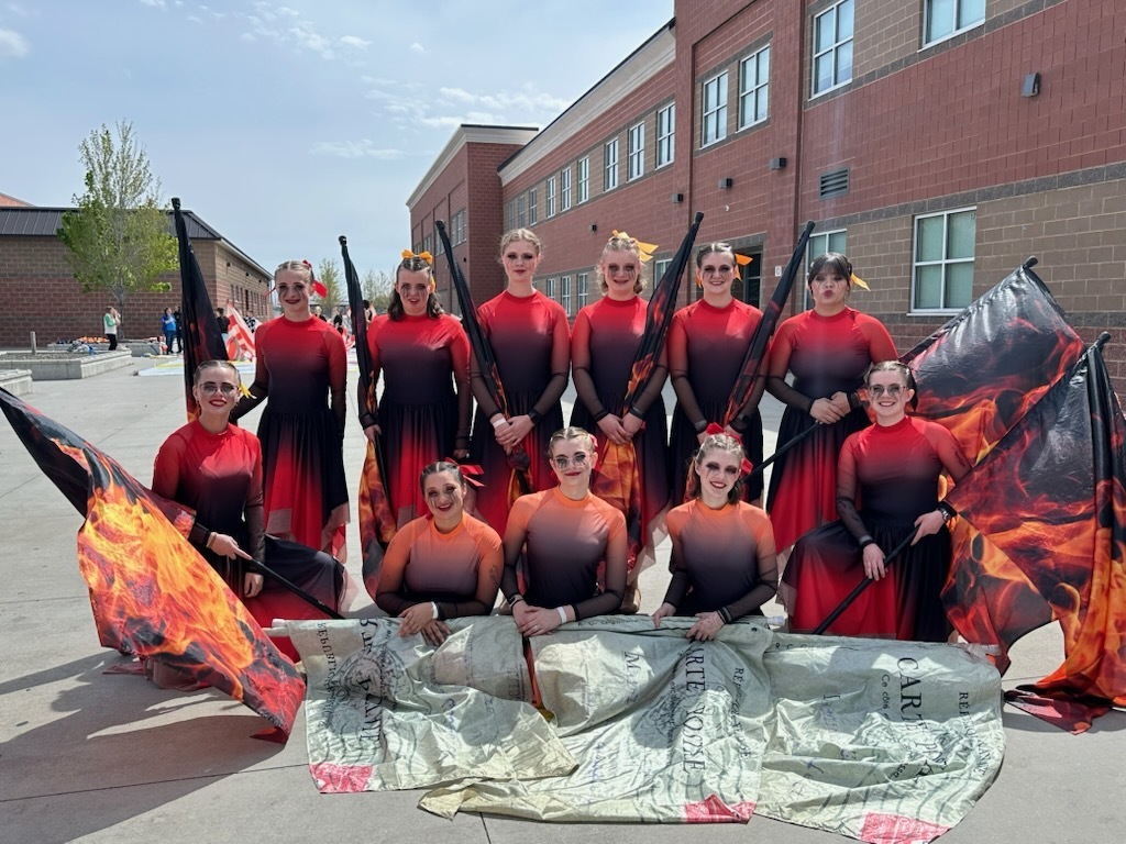 Girls dressed in flame colors pose with large flags outside a building