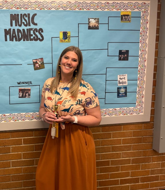 A bulletin board with a "Music Madness" bracket and Mrs. Walker pictured next to the "Winner" slot .