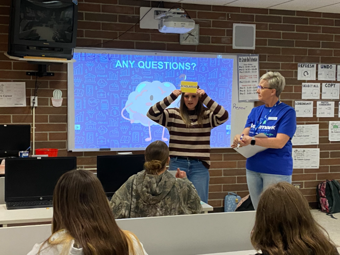 A student standing in front of the class holding a yellow card to her forehead with a word on it to play a game to test the kids about what they learned.