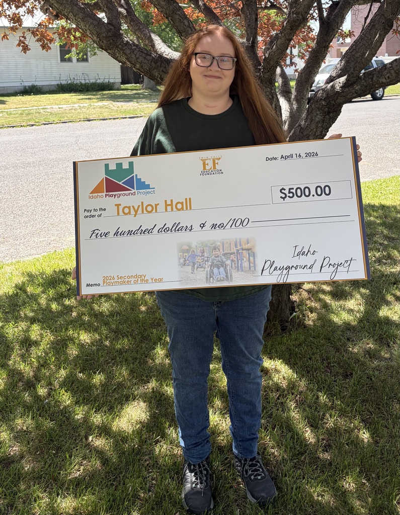 A picture of a staff member standing beneath a tree holding a large check.