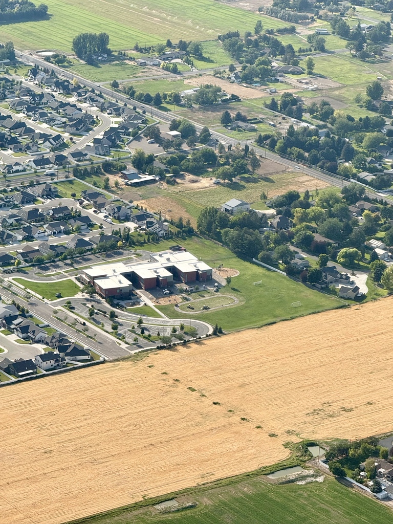 An aerial view of a town shows a mix of residential houses, a large building, and agricultural fields.