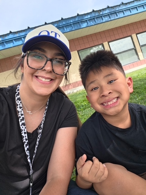 A woman and a boy smile for a selfie in front of a building with windows.