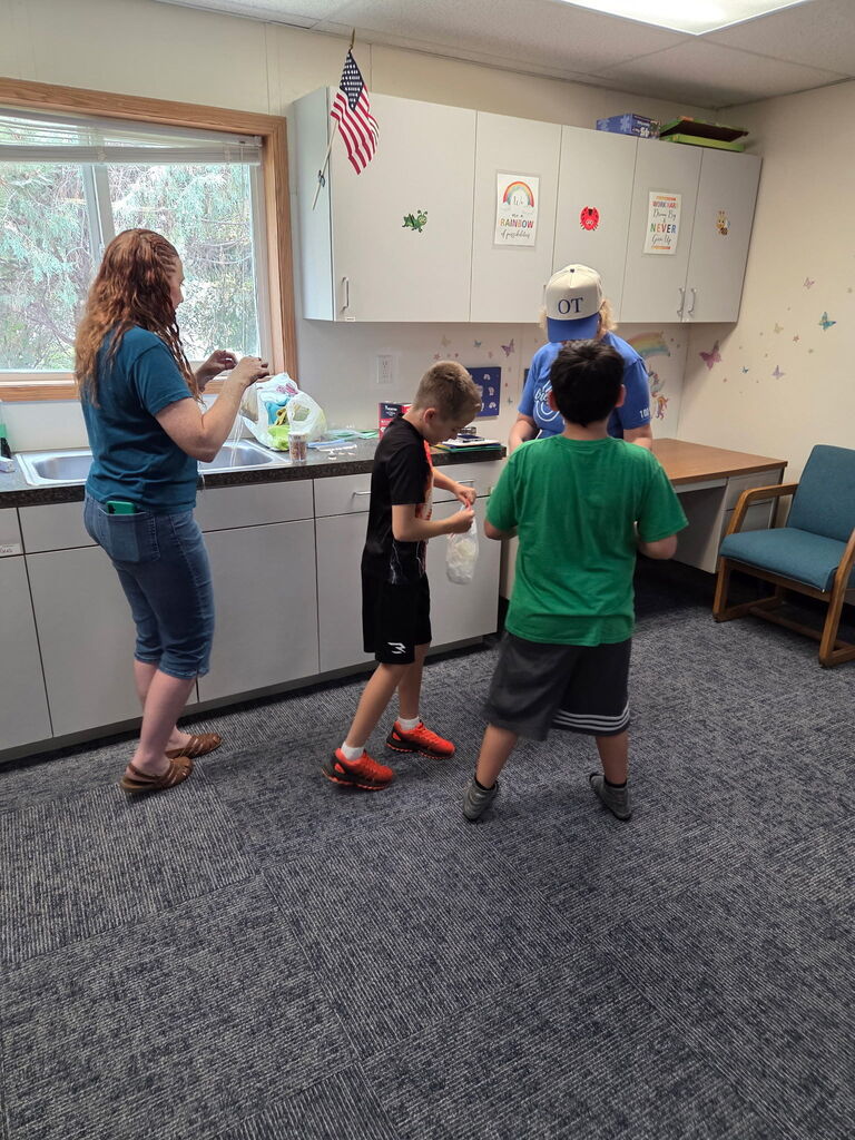 Several people, including children, are in a kitchen area. One child holds a plastic bag.