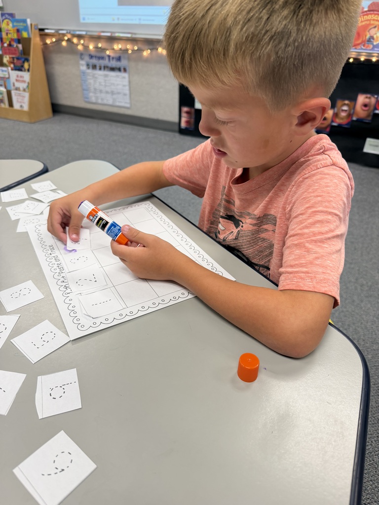 A young boy, wearing a pink shirt, is seated at a table, engaged in an activity with a marker and paper.