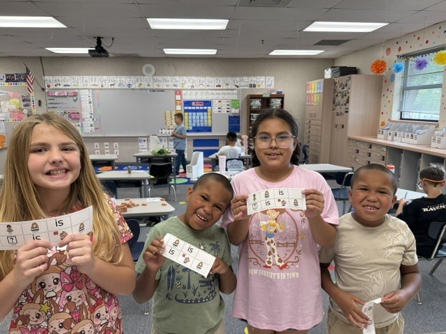 Four children holding up cards with numbers in a classroom. Two girls and two boys.
