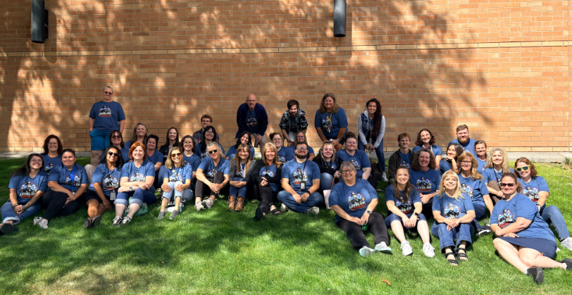 Lincoln Elementary's staff in matching blue shirts sit and standing on grass in front of a brick wall..
