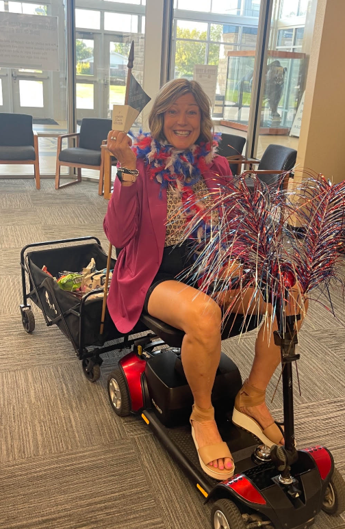 Principal, Nancy Jones, sits on a motorized scooter with a wagon filled with treats attached to the back.