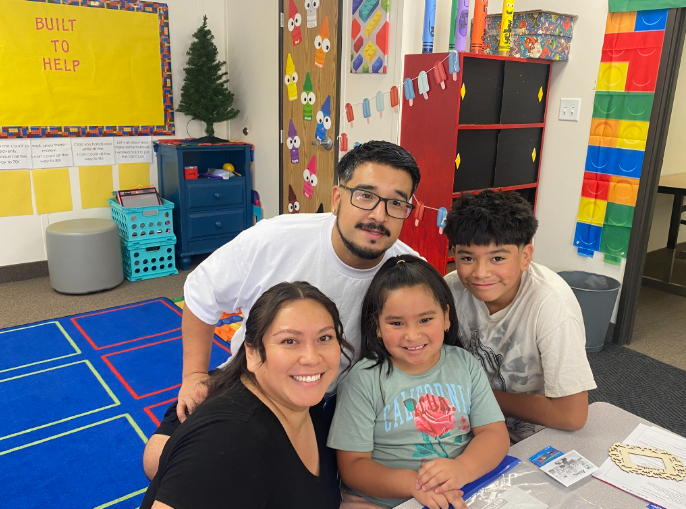 A family of four posing for a picture in a classroom.