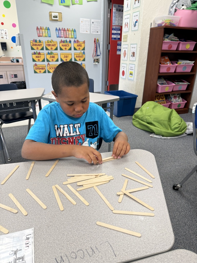 A young boy in a blue t-shirt works with wooden sticks on a table in a classroom.
