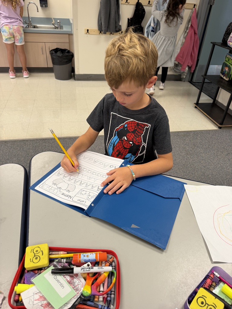 A young boy works on coloring a page at a desk with a blue folder open.