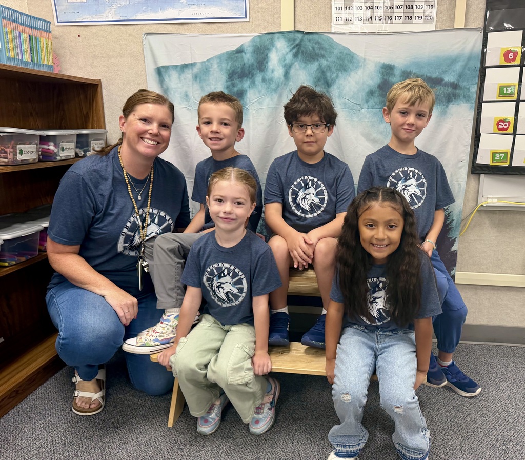 Six children and a woman wear matching blue T-shirts. They sit and kneel on a bench, smiling.