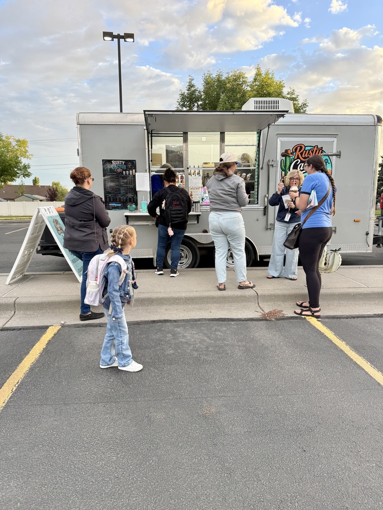 People gather in a parking lot, some in front of a food truck. A streetlight is in the background.