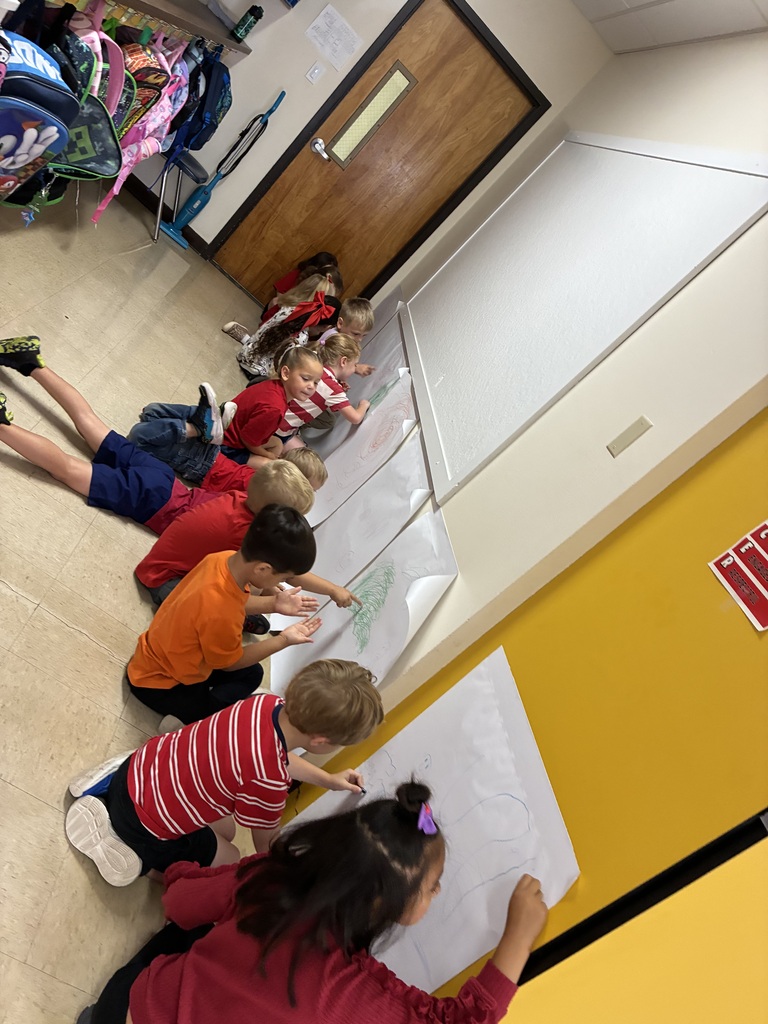 Children seated on the floor, working on a long piece of paper against a yellow wall.