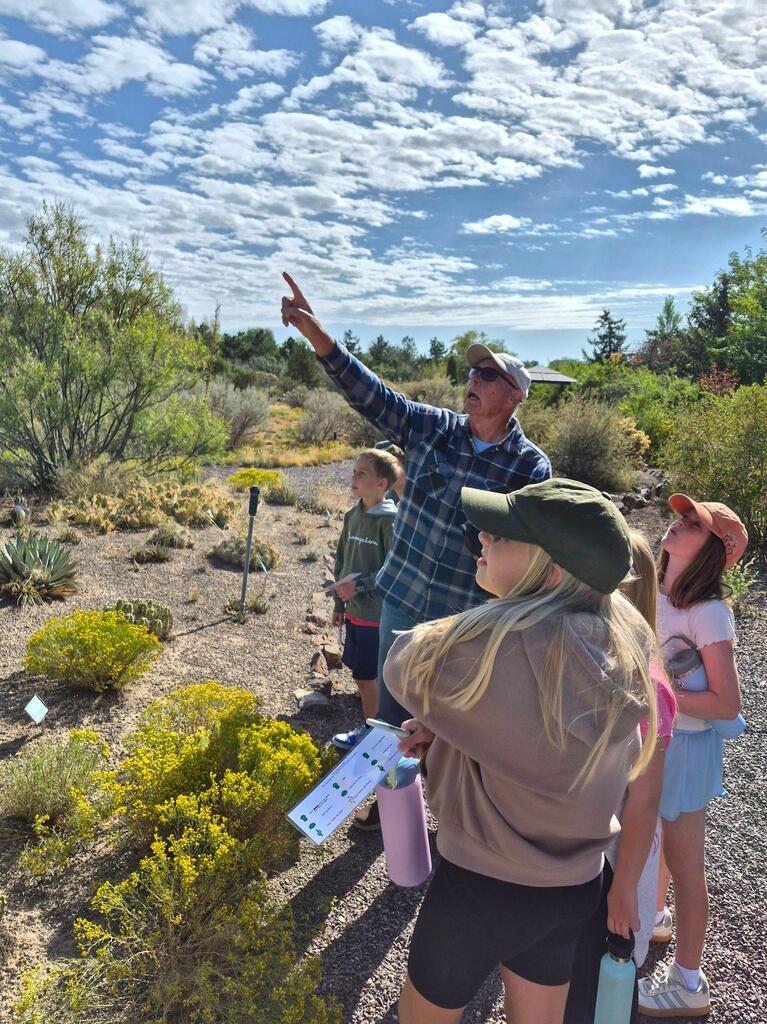 A group of people standing in a field with bushes, one person pointing at something.