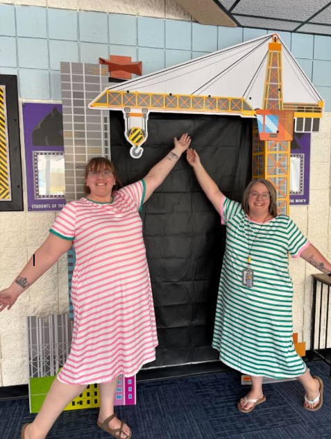 Two women pose for a picture in front of a large construction-themed backdrop.