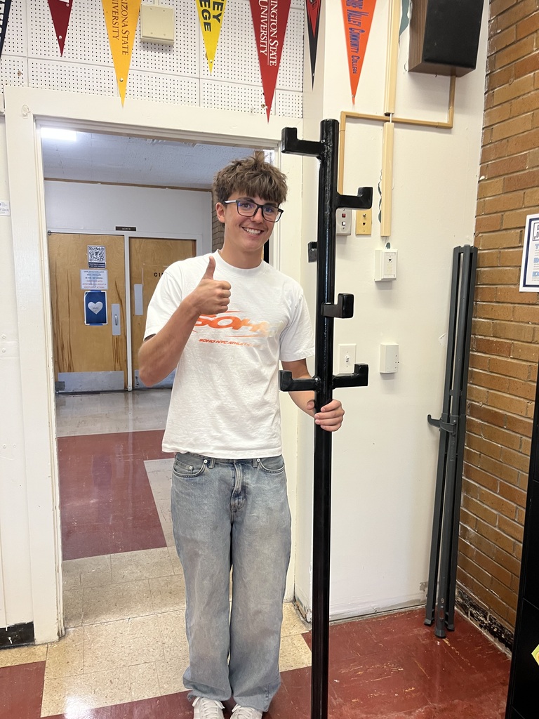 Thumbs up from a student standing near a metal coat rack they made