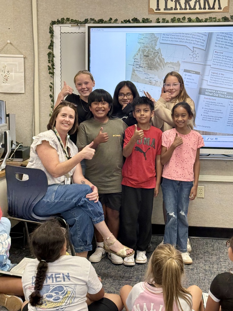A group of children and a woman are standing in front of a screen showing a map.