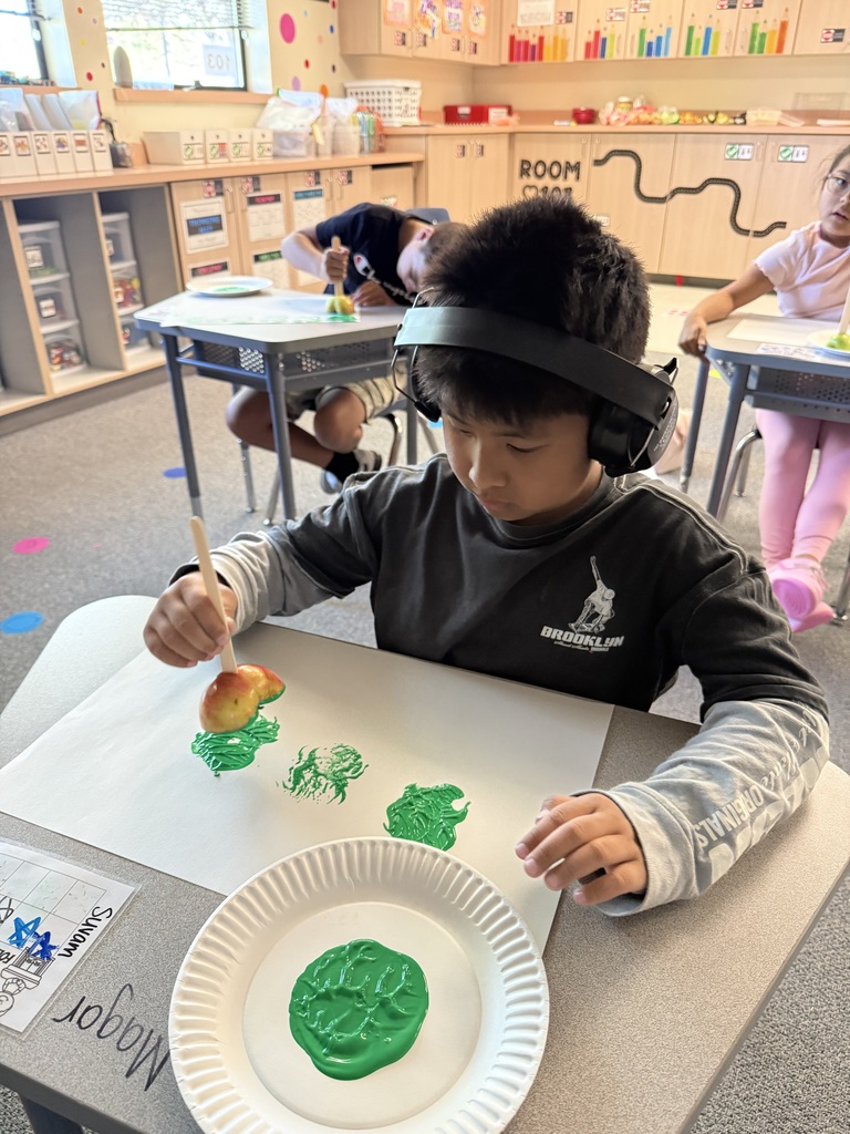 A young boy wearing headphones is painting green on a paper plate at a table.