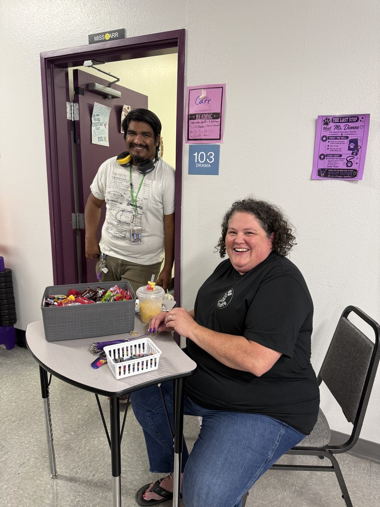 A woman smiles at a table with a box of candy while a man stands behind her.