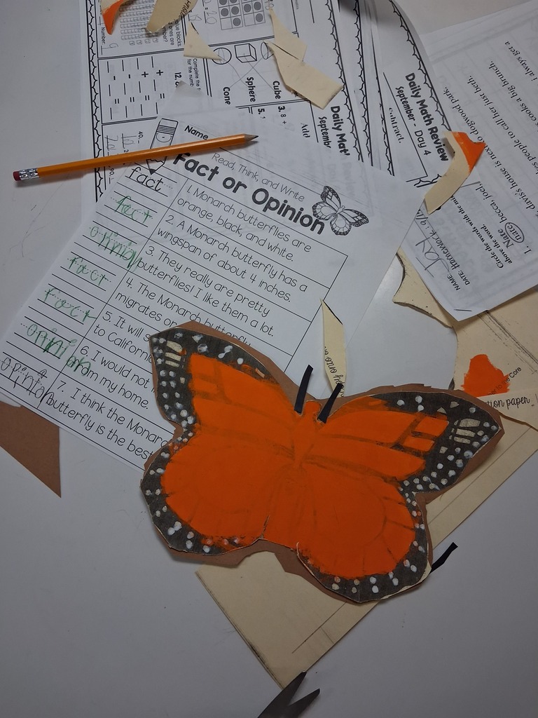 A classroom setting with papers, a pencil, and a butterfly cutout. Papers have text and images related to facts or opinions.