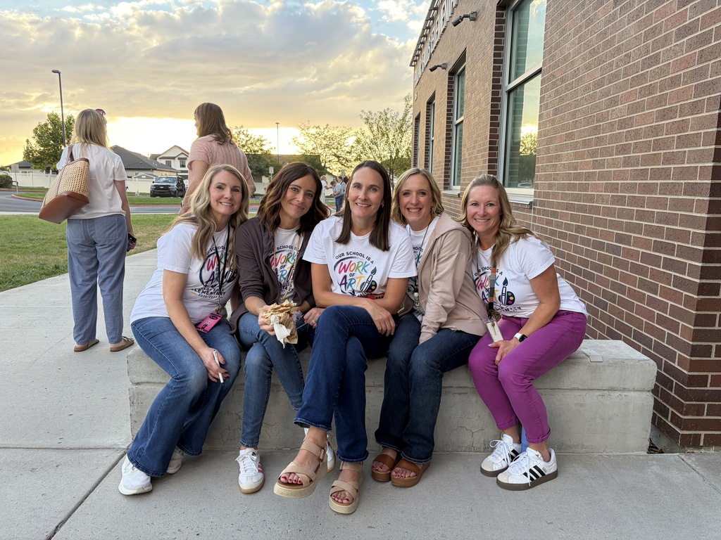 Five women in white t-shirts and various pants, sitting on a bench outside a brick building.