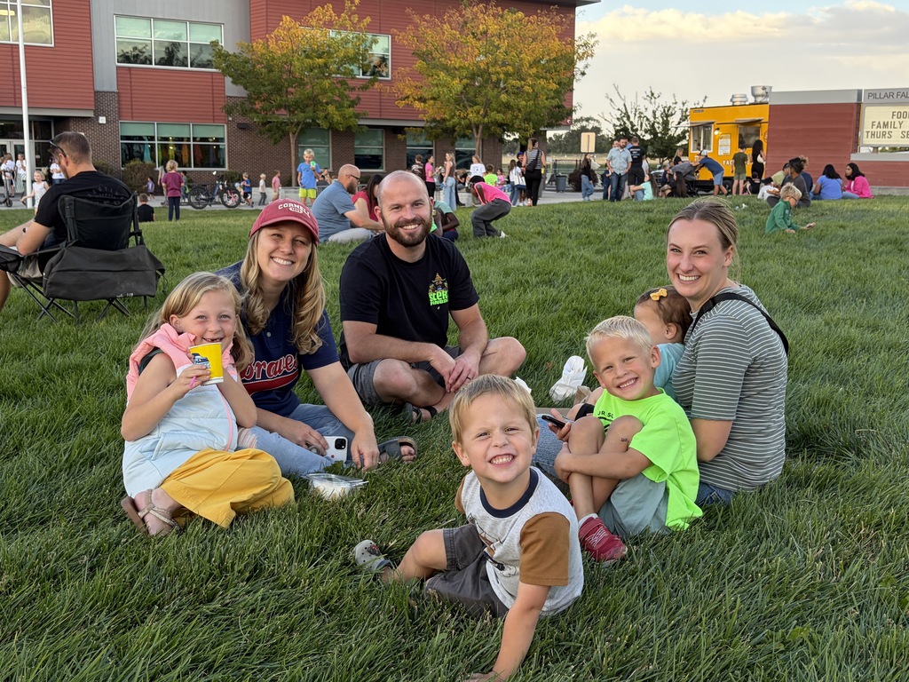 A family sits on grass outside a building. A man, woman, and four children are smiling.
