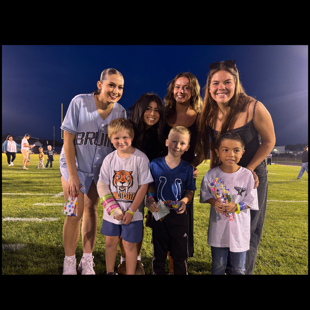 A group of people on a football field, including several young children and adults, at night.