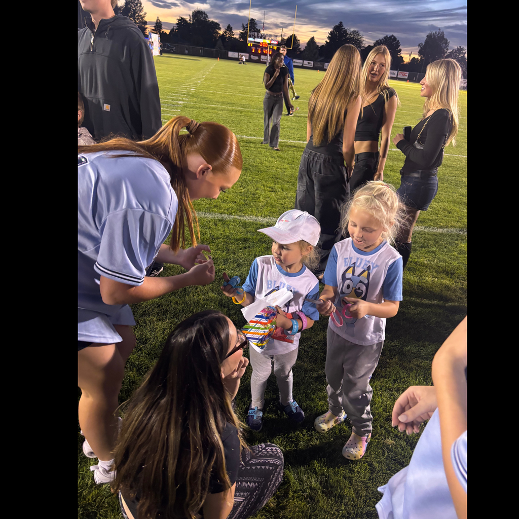 Adults and children gathered on a grassy field. One woman kneels to give a child a gift.