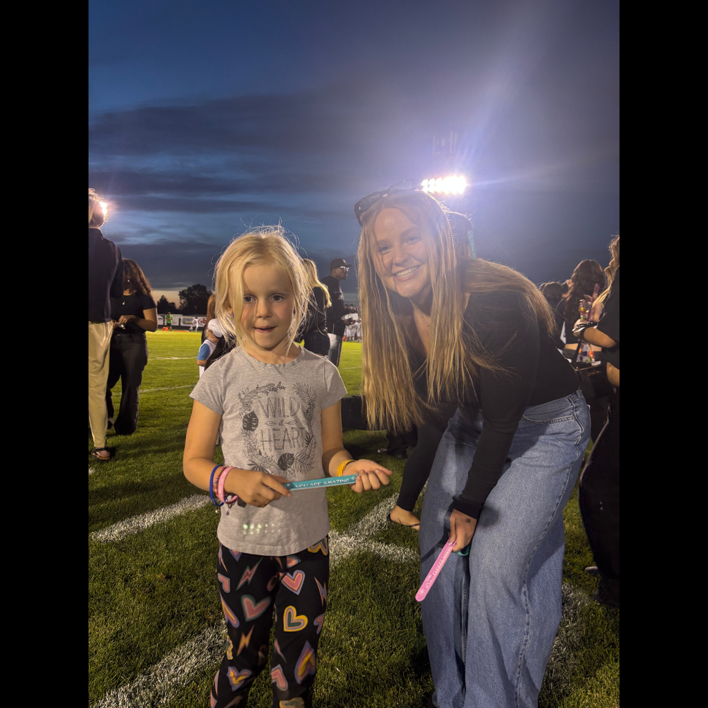 Two people on a field. A woman holds a light stick. A child stands holding a stick, looking at the camera.