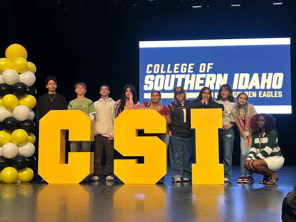 A group of students stand behind "CSI" letters on a stage with yellow balloons.