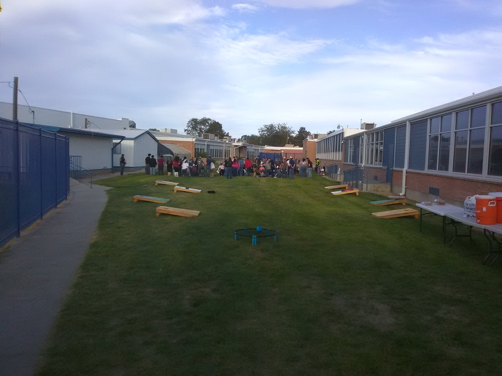 A group of people are standing on a grassy field with a blue fence and a building.