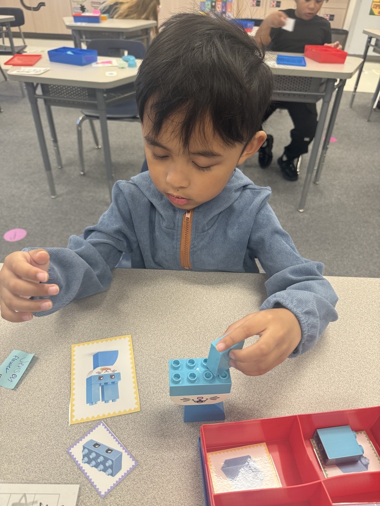 A child sitting at a desk plays with small blue and red blocks, focusing on arranging them.