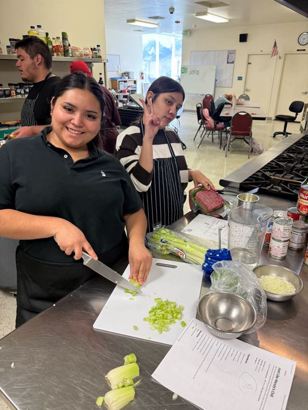Two people at a kitchen counter, one cutting celery, and the other making a peace sign.