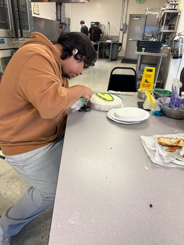 Person in a kitchen decorating a cake with green and yellow icing on a table.