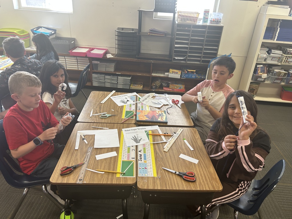 Kids are sitting at a desk, working on crafts with scissors, paper, and other materials.