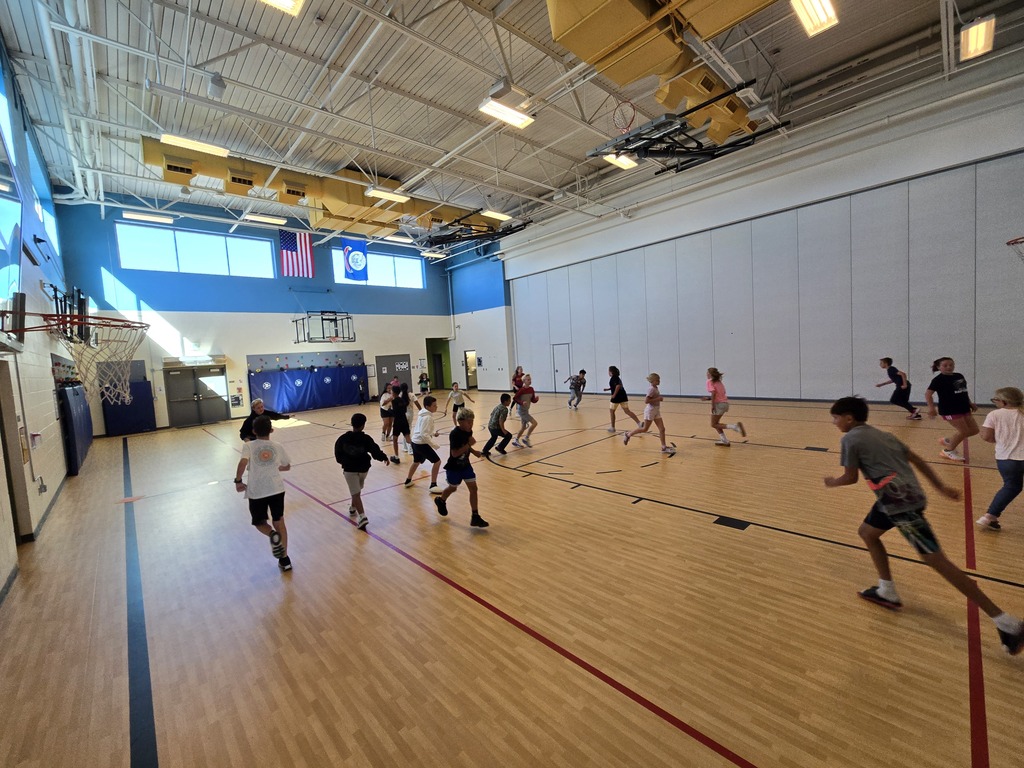 A group of children running in a gymnasium with wooden floors and an open ceiling.