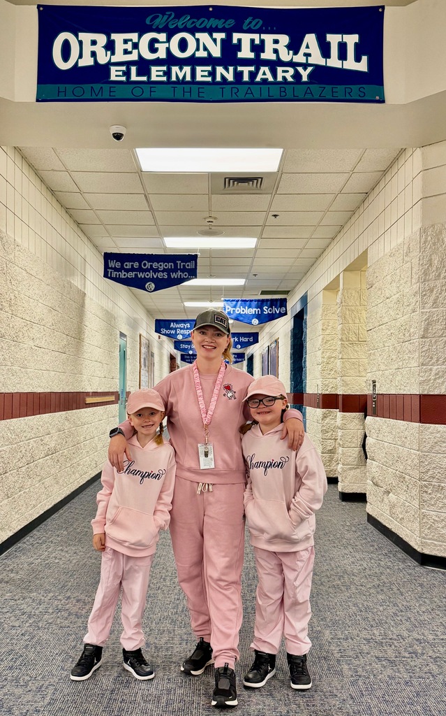 A woman in pink scrubs and two children in matching pink outfits stand in a hallway. A blue sign reads "Oregon Trail Elementary".