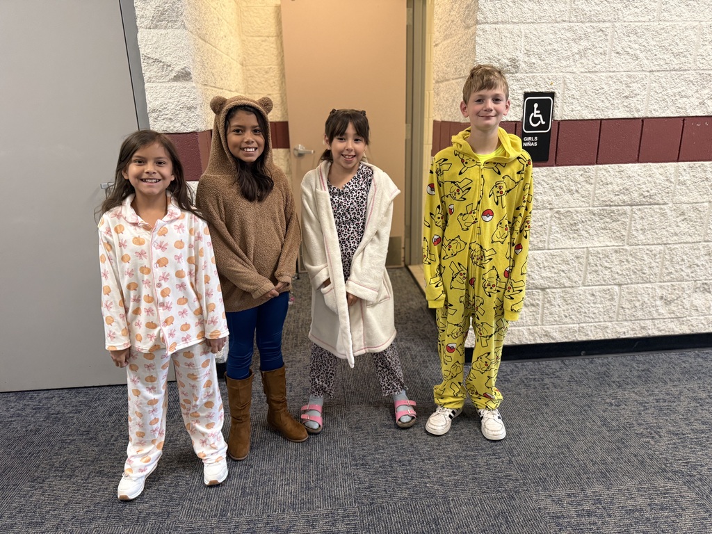 Four children, two girls and two boys, stand close together in a hallway. They wear different pajamas, with two having boots.