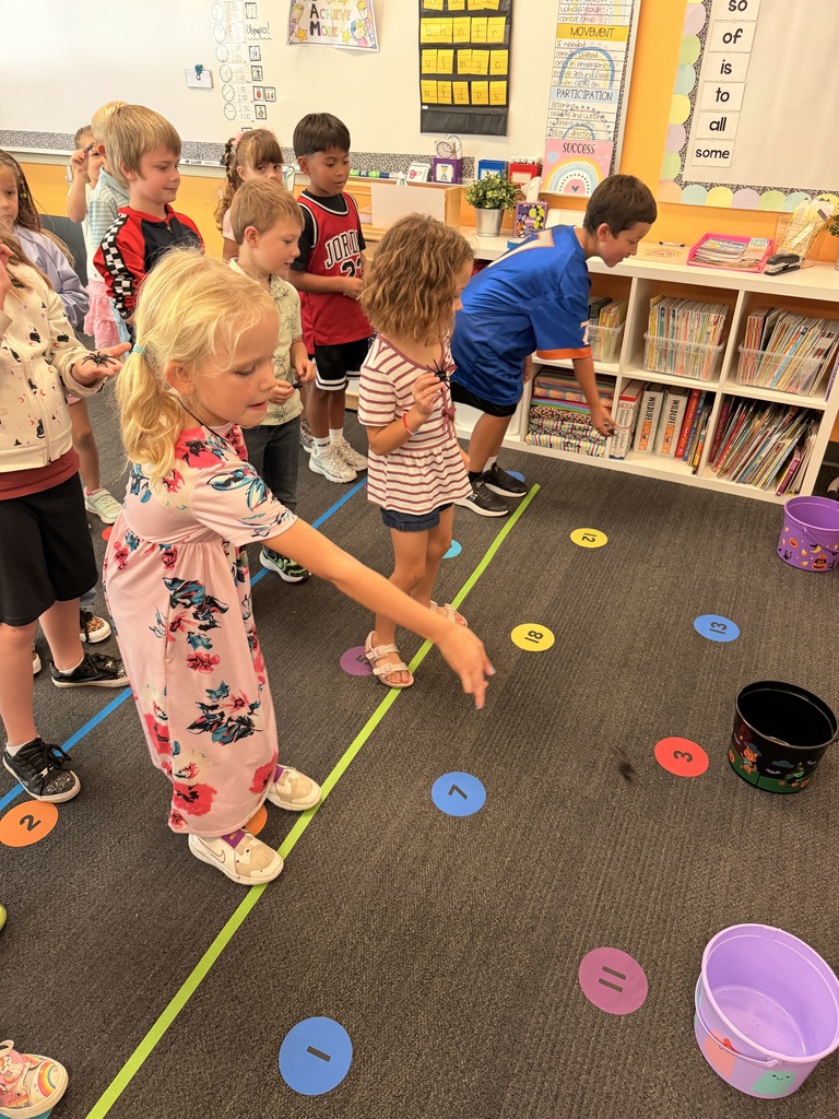 A group of young children stand on a floor with circles. A girl throws a ball.