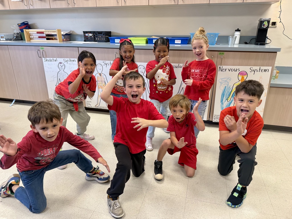 A group of children in red t-shirts and pants, some kneeling, others standing, smiling and posing for a picture.