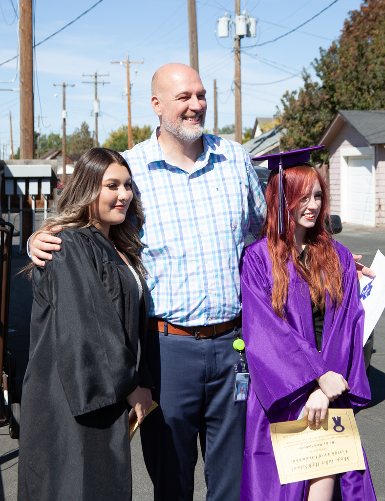 Two women in caps and gowns stand with a man in a blue shirt, smiling.