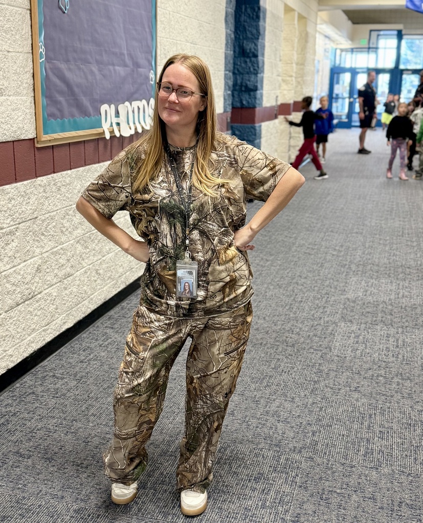 Woman in camouflage uniform with ID card standing in hallway, several children walking in the background.
