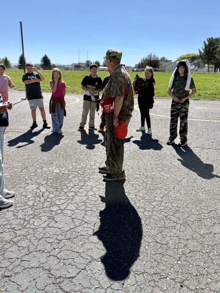 A group of people in casual clothing, with one in camouflage, stand on cracked asphalt. Shadows are cast on the ground.