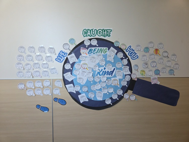 A bulletin board shows a large magnifying glass with "Caught Being Kind" in center. Surrounding it are various speech bubbles with faces.