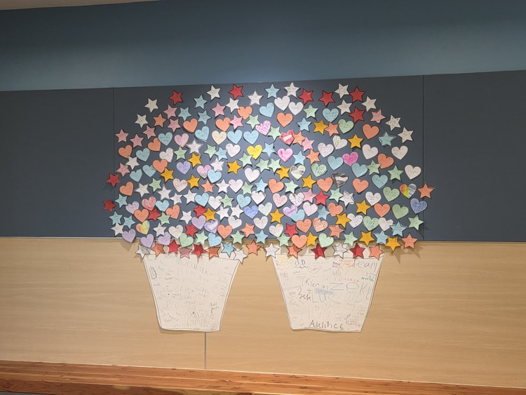 Display of colorful paper hearts and stars arranged in two vases on a wall.