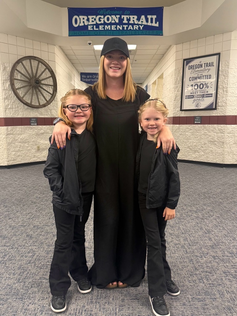 A woman with two young girls. They are all dressed in black, standing in a hallway with an Oregon Trail Elementary sign.